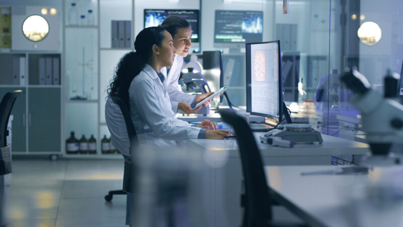 focused-serious-medical-scientists-analyzing-research-scans-on-a-computer-working-late-in-the-laboratory-lab-workers-examine-and-talk-about-results-from-a-checkup-while-working-overtime